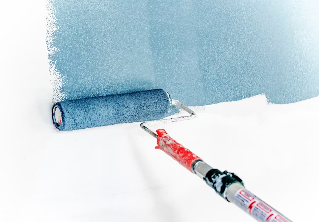 Painter in white coveralls rolling paint onto an interior wall